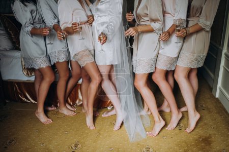 Téléchargez les photos : The morning of the bride with her friends at the wedding. girls stand barefoot in peignoirs in the room - en image libre de droit