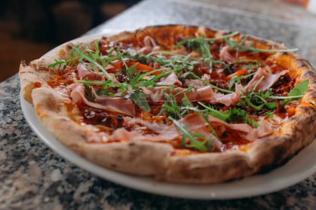 Foto de Pizza con jamón y ensalada de rúcula sobre mesa de madera. - Imagen libre de derechos