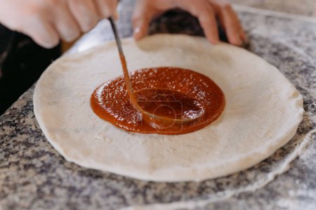 Photo for Female hand smudging sauce on pizza dough, closeup - Royalty Free Image