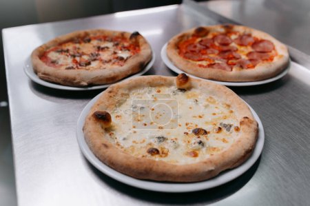 Foto de Cheese, meat and tomato pizza on a metal table. - Imagen libre de derechos
