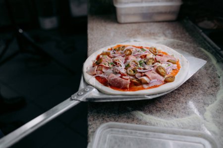 Téléchargez les photos : Préparation de pizza italienne traditionnelle. Chef tient longue pelle irob pour pizza, pâte à pâtisserie avec pâtes et fromage dans un four professionnel. - en image libre de droit