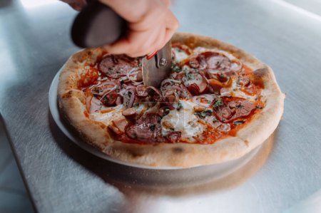 Téléchargez les photos : Gros plan main de chef boulanger en uniforme blanc coupe pizza à la cuisine - en image libre de droit