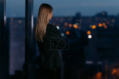 Photo for A woman is standing in the office, looking at the night city. - Royalty Free Image