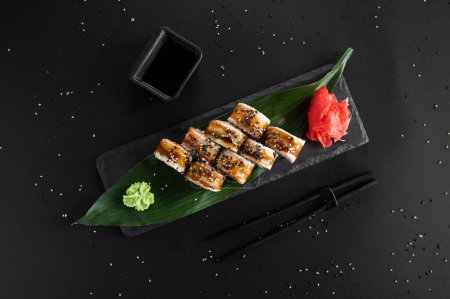 Téléchargez les photos : Rouleau de sushi avec anguille, sésame et fromage Philadelphie sur fond noir. Nourriture japonaise. - en image libre de droit