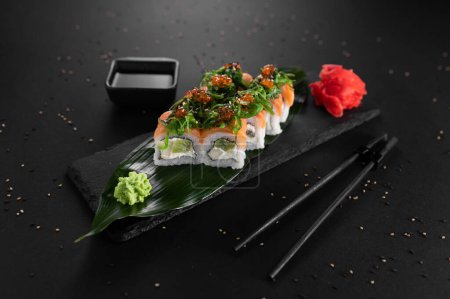 Foto de Set de sushi con pescado rojo, caviar, algas, queso y kiwi sobre fondo negro. - Imagen libre de derechos