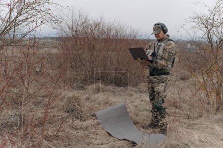 Téléchargez les photos : Militaire se tient en camouflage et travaille avec un ordinateur portable. - en image libre de droit