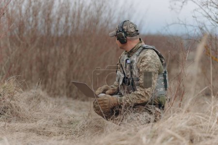 Photo for Military man stands in camouflage and works with a laptop. - Royalty Free Image