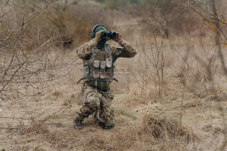 Foto de Un soldado camuflado sostiene prismáticos. militar sosteniendo prismáticos. soldado en el campo - Imagen libre de derechos