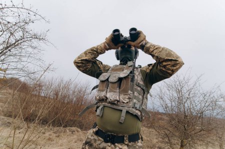 Téléchargez les photos : Un soldat en camouflage tient des jumelles. militaire tenant des jumelles. soldat sur le terrain - en image libre de droit