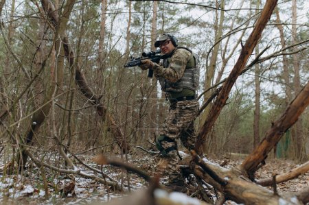 Téléchargez les photos : Militaire en uniforme de camouflage sur les branches des arbres, dans une embuscade avec une arme, une mitrailleuse. des actions militaires un soldat dans la forêt. - en image libre de droit
