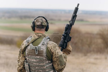 Foto de Un soldado con una ametralladora se para con la espalda en uniforme militar - Imagen libre de derechos