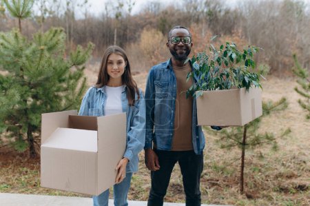 Téléchargez les photos : Une jeune famille heureuse emménage dans une maison. Un homme et une femme noirs tiennent des boîtes en carton pour bouger, souriant. boîtes mobiles - en image libre de droit