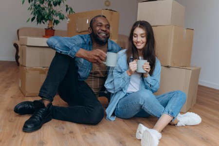 Photo for Couple moving in house. interracial couple sitting near cardboard boxes - Royalty Free Image
