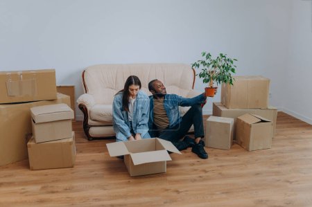 Téléchargez les photos : Couple emménageant dans la maison. couple interracial assis près de boîtes en carton - en image libre de droit