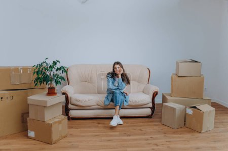 Foto de Mujer empacando para mudarse a un apartamento nuevo. una mujer se sienta en un sofá cerca de cajas - Imagen libre de derechos