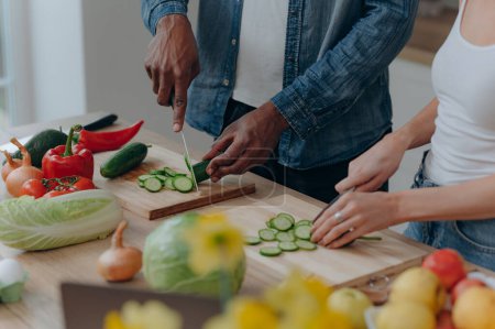 Téléchargez les photos : Gros plan d'une planche à découper avec les mains d'un couple coupant des légumes ensemble dans la cuisine. Aliments végétariens sains - en image libre de droit