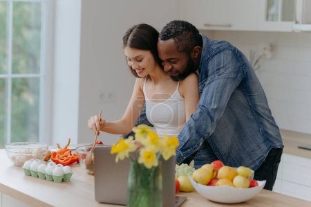 Photo for A happy interracial couple preparing food in the kitchen. African-American man and a Caucasian woman prepare a salad - Royalty Free Image