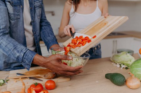Photo for Close up of a cutting board with the hands of a couple cutting vegetables together in the kitchen. Vegetarian healthy food - Royalty Free Image