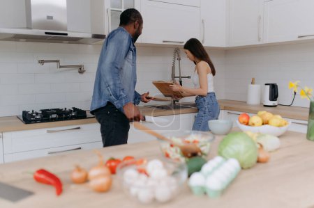 Téléchargez les photos : Un jeune couple heureux est occupé dans la cuisine. Un homme noir et une jeune fille font la vaisselle - en image libre de droit
