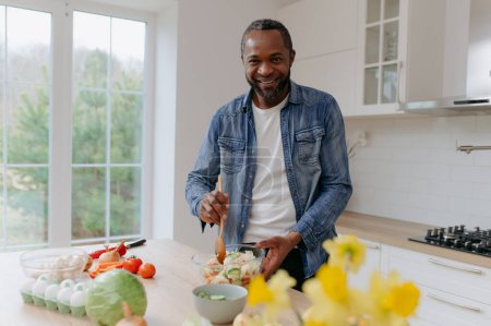 Foto de Un hombre afroamericano prepara una ensalada de verduras, una comida saludable. - Imagen libre de derechos