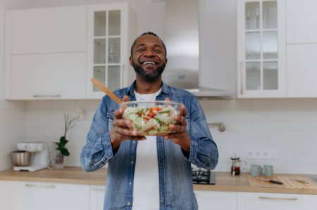 Téléchargez les photos : Un Afro-Américain tient une salade dans la cuisine. - en image libre de droit