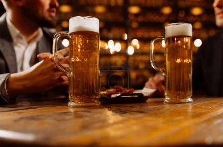 Foto de Dos vasos de cerveza en manos de hombres, amigos en un bar, una noche en un pub - Imagen libre de derechos