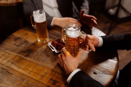 Foto de Dos vasos de cerveza en manos de hombres, amigos en un bar, una noche en un pub - Imagen libre de derechos