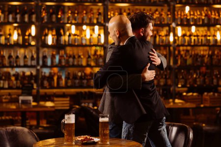 Photo for Men hug when meeting in a pub. friends met in a bar after work. - Royalty Free Image