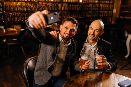 Foto de Amigos beber cerveza y tomar selfie con teléfono inteligente en el bar o pub. amistad masculina - Imagen libre de derechos