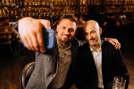 Foto de Amigos beber cerveza y tomar selfie con teléfono inteligente en el bar o pub. amistad masculina - Imagen libre de derechos