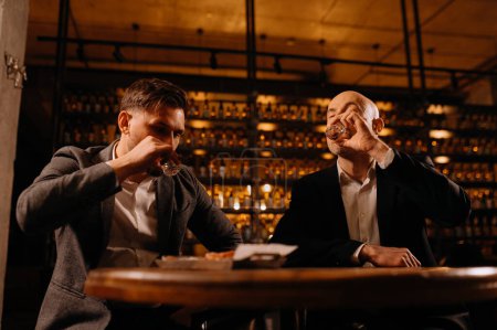 Téléchargez les photos : Des amis se grillent les uns les autres avec des photos de vodka pendant qu'ils passent une soirée ensemble au pub - en image libre de droit