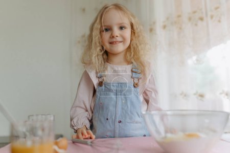 Photo for Little girl with ingredients for baking. The child prepares food, cookies. The kid has fun, learns to cook and plays in the kitchen. - Royalty Free Image