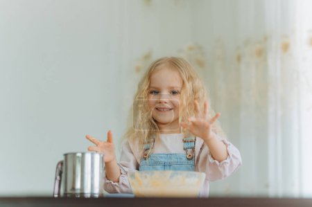 Foto de Niña con ingredientes para hornear. El niño prepara la comida, las galletas. El niño se divierte, aprende a cocinar y juega en la cocina. - Imagen libre de derechos