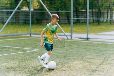 Téléchargez les photos : Un joueur de football garçon en uniforme vert court avec le ballon sur le terrain de football - en image libre de droit