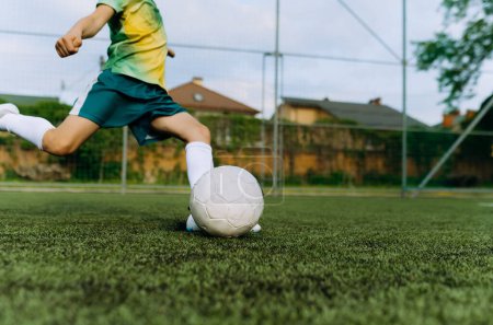 Foto de Un pequeño jugador de fútbol patea la pelota en el gol. Niño jugando juego de fútbol - Imagen libre de derechos