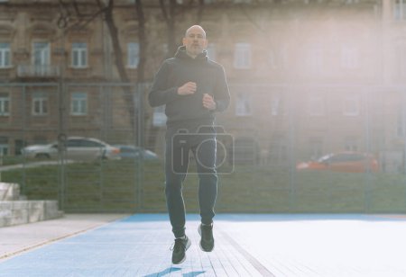 Foto de Un hombre calvo corre en un campo de deportes azul - Imagen libre de derechos