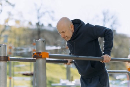 Photo for Bald man in sportswear is training outdoors with parallel bars - Royalty Free Image