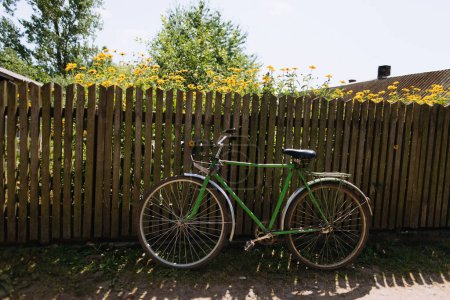 Photo for An old bicycle is placed on a wooden fence. green bicycle on a background of yellow flowers - Royalty Free Image