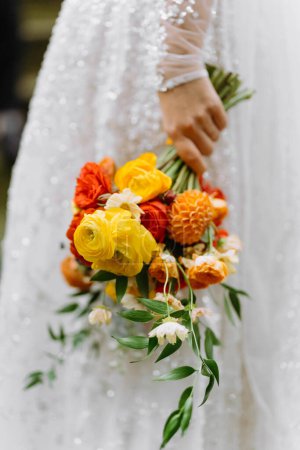 Téléchargez les photos : Mariée en robe de mariée blanche tenant un bouquet de fleurs vives. un bouquet de fleurs jaunes, rouges et orange - en image libre de droit