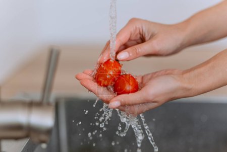 Foto de Primer plano de verduras frescas. Las manos femeninas lavando tomates cherry con el agua en la cocina. - Imagen libre de derechos