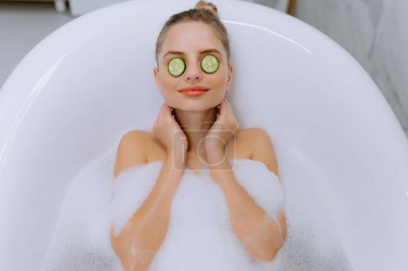 Photo for Close up female face with cucumber slices on eyes. Beautiful young woman rest in bubble bathtub. Attractive girl relaxing with facial mask. Clean pure skin spa time. Beauty health care - Royalty Free Image