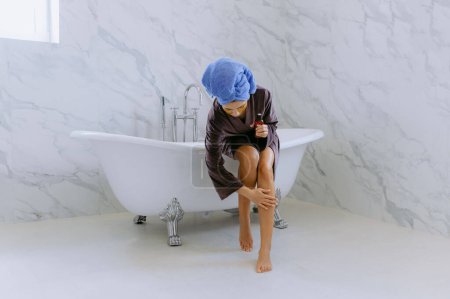 femme applique une crème hydratante sur ses jambes dans la salle de bain. femme dans la salle de bain toucher les pieds jouissant d'une peau lisse après l'épilation ou l'épilation à la maison en appliquant hydratant le corps