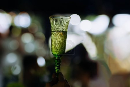 Foto de Un hombre sostiene una copa de vino llena de vino blanco. Una mujer hace un brindis. Copa verde con vino blanco. un brindis en la celebración - Imagen libre de derechos