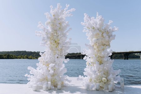 Beautiful wedding arch decorated with white rose flowers installed on the river embankment in the city. Wedding ceremony in sunny summer day. white wedding arch