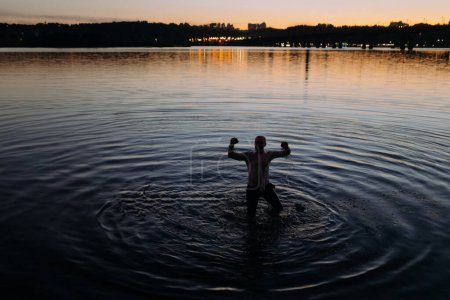 Téléchargez les photos : Un homme joyeux nage dans la rivière le soir. l'homme est tombé dans la rivière. l'homme a nagé à terre. un survivant chanceux dans l'eau - en image libre de droit