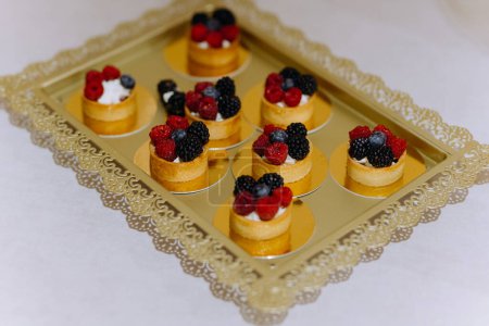 Foto de Un conjunto de mini pasteles dulces con bayas, frambuesas, arándanos, fresas. buffet dulce. Pasteles de frutas surtidos para vacaciones - Imagen libre de derechos