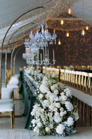 Photo for Luxury wedding banquet hall. Table decorated for a wedding celebration. Bouquets of white and peach flowers, vintage decor. White bright room, an arch of rose flowers - Royalty Free Image