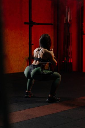 Foto de Sporty woman squats in the gym. A sexy girl squats in the gym, shakes her ass - Imagen libre de derechos