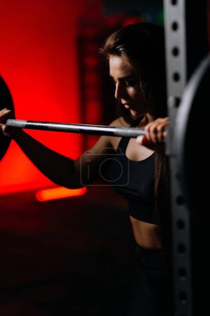 Foto de Sporty woman squats in the gym. A sexy girl squats in the gym, shakes her ass. place for text - Imagen libre de derechos