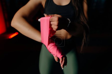 Foto de La mujer está envolviendo las manos con envolturas de boxeo rosa. Aislado en negro con uñas rojas. Mano y puño fuertes, listos para la lucha y el ejercicio activo. Matte lavado imagen - Imagen libre de derechos